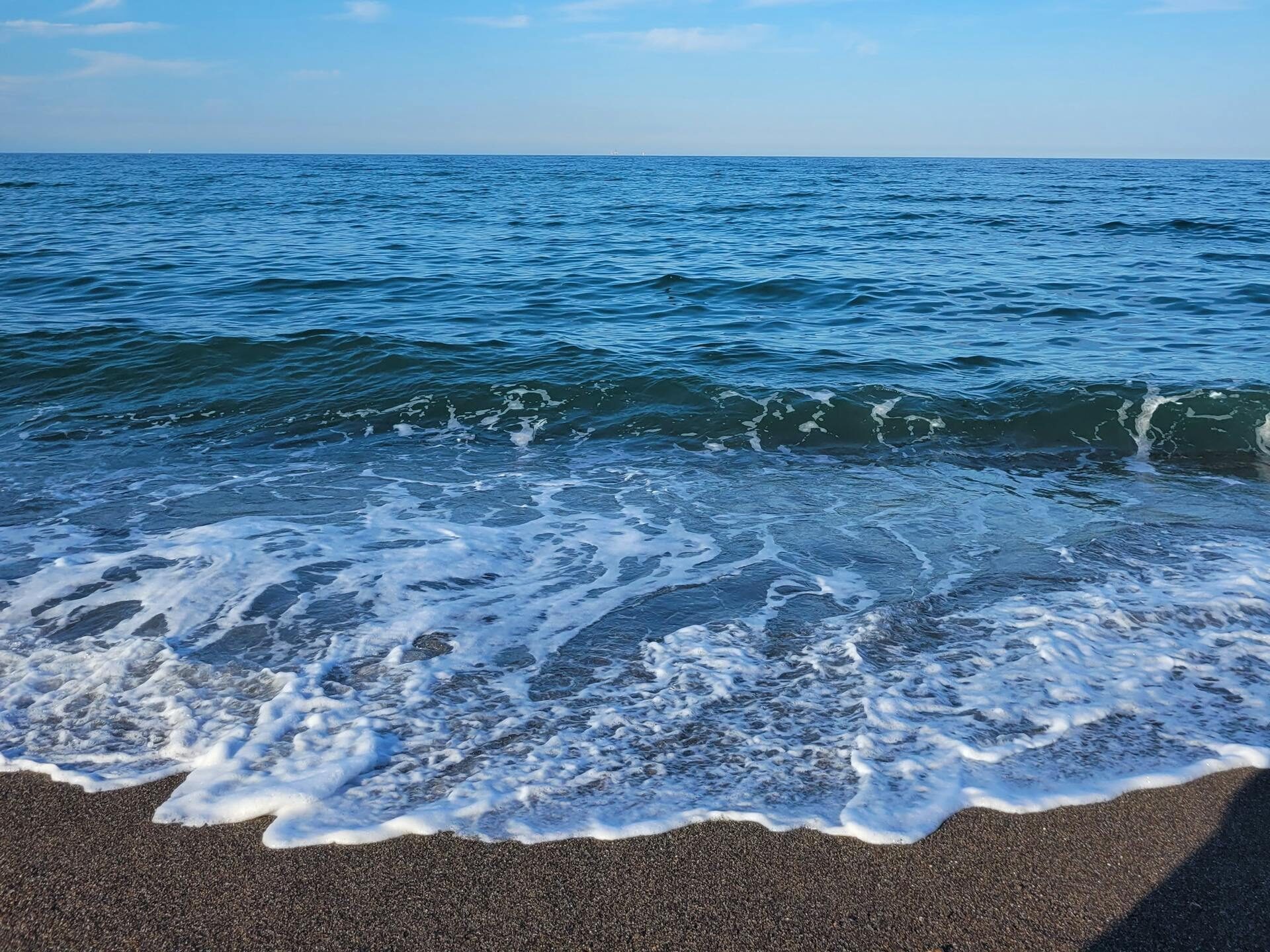 Calm waves gently hitting the sandy beach under a bright blue sky